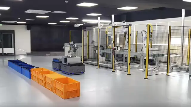 Mobile robots beside storage bins and fenced equipment in an industrial robotics facility